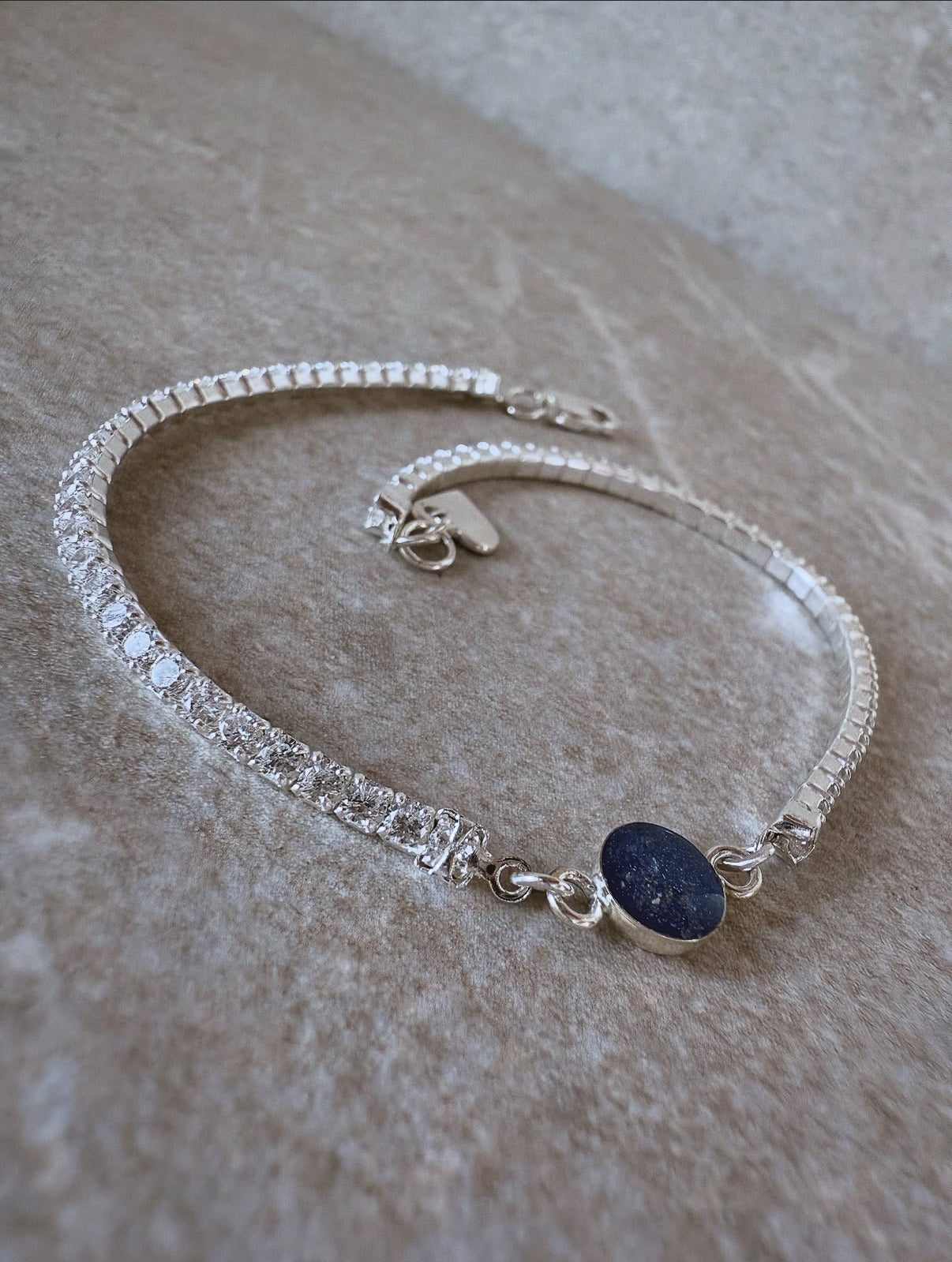 Silver bracelet with a dark blue stone on a beige surface