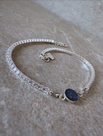 Silver bracelet with a dark blue stone on a beige surface